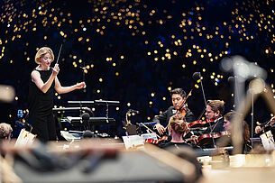 Dirigentin Joana Mallwitz und Staatsphilharmonie Nürnberg mit Wunderkerzen im Hintergrund